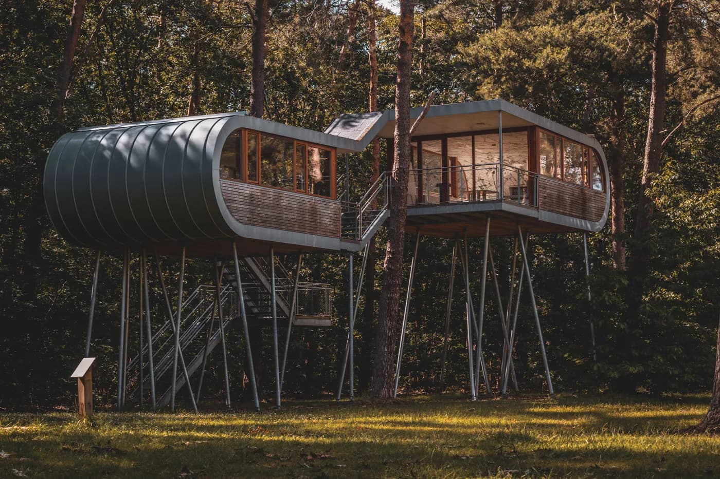 BookNoFees-voorbeeldfoto: twee moderne boomhutten op palen met metalen trappen tussen de bomen in het bos