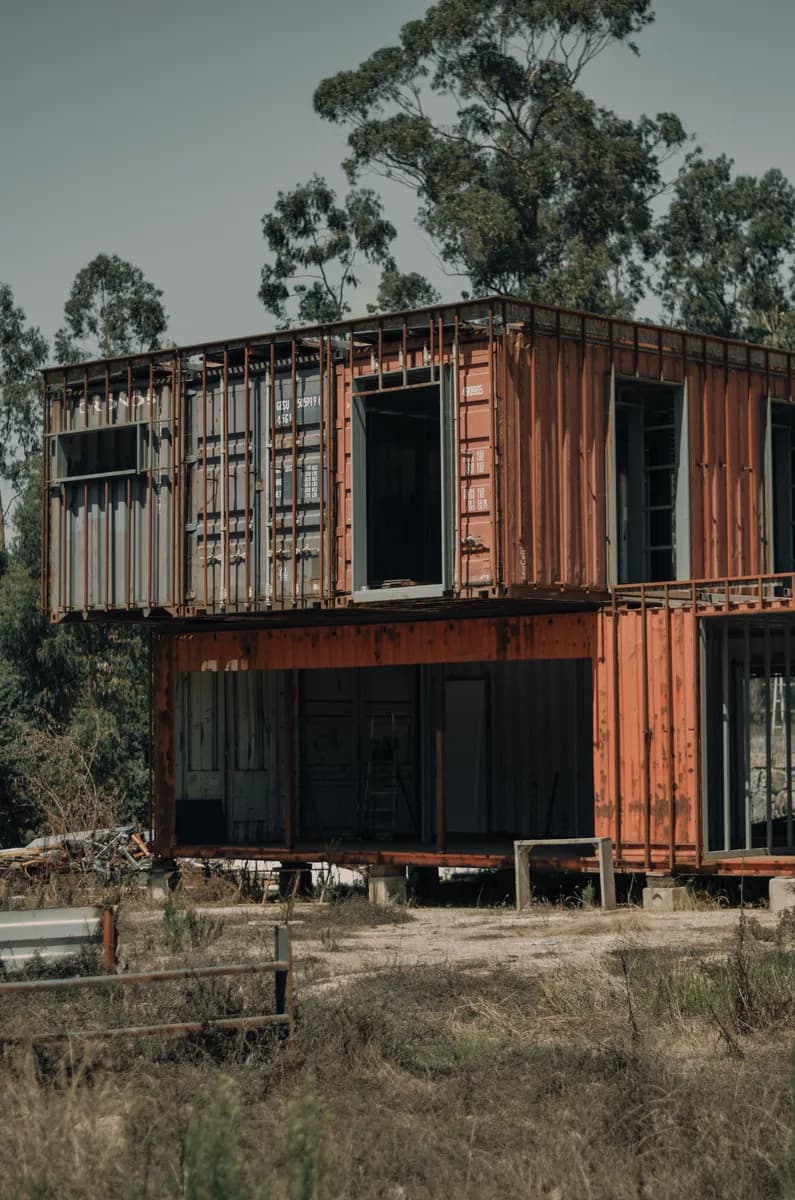 Exemple d'image BookNoFees : maison-conteneur à deux étages avec de grandes fenêtres, nichée parmi les arbres