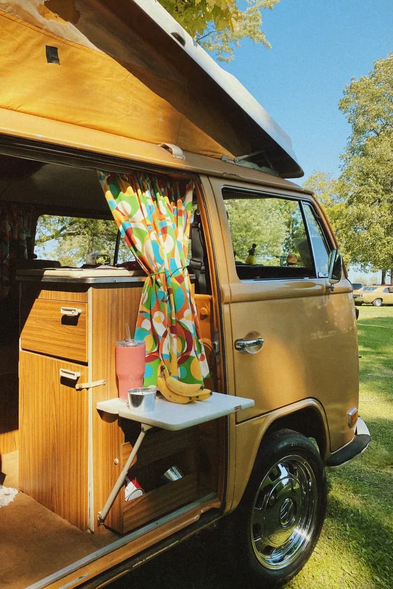 BookNoFees-voorbeeldfoto: Open gele camperbus met houten inrichting en kleurrijke gordijnen in de zon