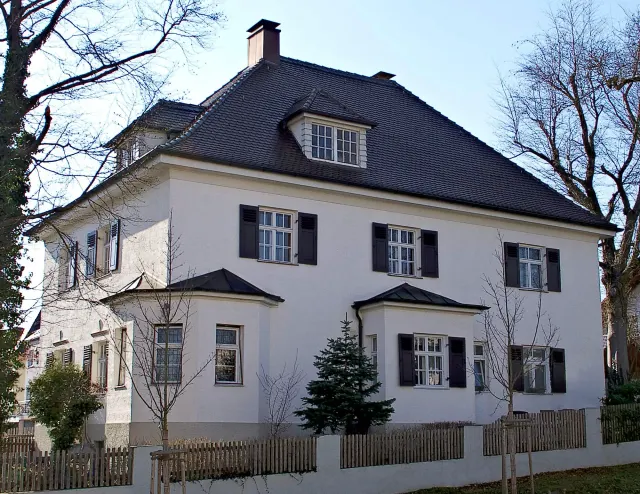 BookNoFees: Ferienwohnung in Friedberg, Bayern, Deutschland – Außenansicht eines weißen, zweistöckigen Hauses mit dunklen Fensterläden, einer Dachgaube und einem Holzzaun