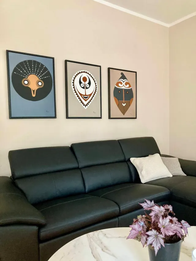 BookNoFees: Ferienwohnung in Friedberg, Bayern, Deutschland – Wohnzimmer mit schwarzem Ledersofa und drei gerahmten Maskenbildern