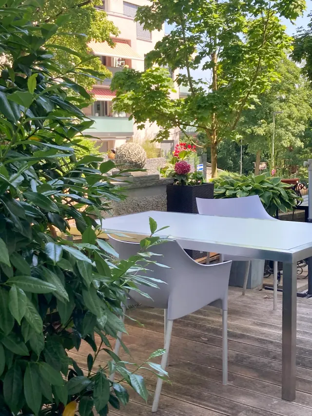 BookNoFees: Ferienwohnung in Friedberg, Bayern, Deutschland – Terrasse mit weißem Tisch und Stühlen, umgeben von üppig grünen Pflanzen