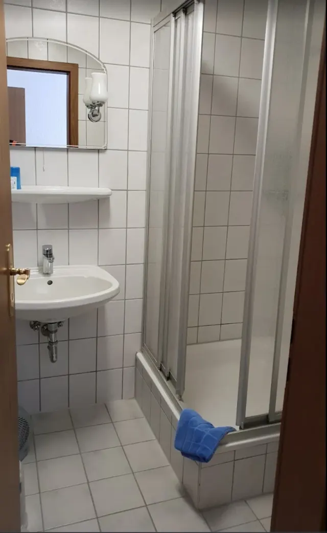 BookNoFees : location de vacances à Schönfeld, Saxe, Allemagne – Salle de bains avec lavabo blanc, baignoire équipée d'une paroi de douche et serviette bleue