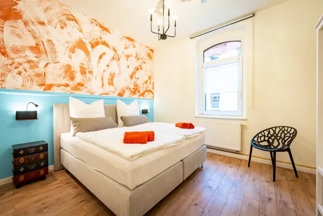 BookNoFees: vakantiehuis in Magdeburg, Duitsland – Slaapkamer met tweepersoonsbed, oranje muurschildering en zwarte stoel