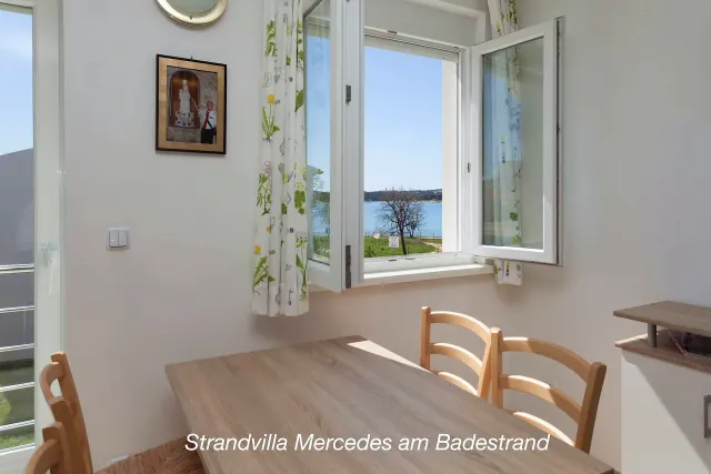 BookNoFees: vakantiehuis in Medulin – Eethoek met houten tafel en open raam met uitzicht op het water