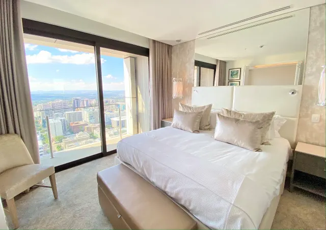 BookNoFees: vakantiehuis in Sandton – Slaapkamer met kingsize bed en een raam van vloer tot plafond met uitzicht op de skyline van de stad