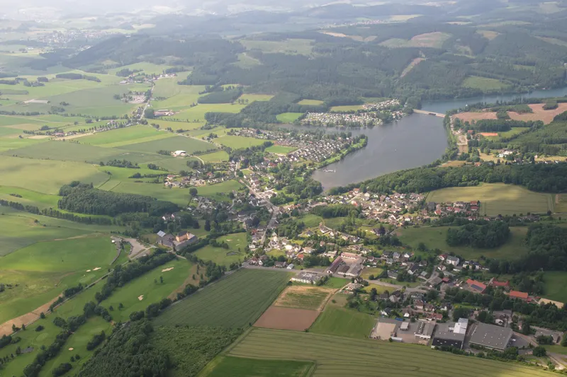 Der Sorpesee aus der Vogelperspektive, mit dem Dorf Amecke an seinem Ostufer und den bewaldeten Hügeln des Sauerlands im Hintergrund