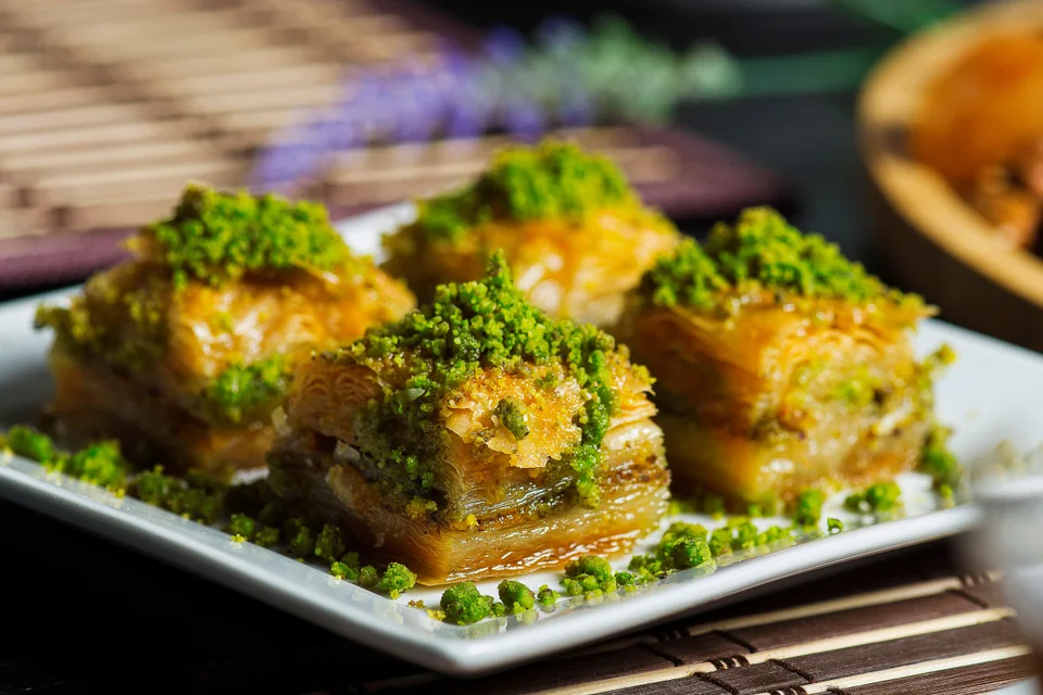 BookNoFees: Voorbeeldfoto: Vier stukken gelaagde baklava, gegarneerd met gemalen pistachenoten op een wit bord