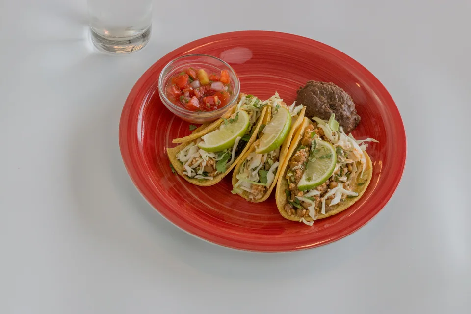 BookNoFees: Voorbeeldfoto: Drie taco's gegarneerd met schijfjes limoen en salsa op een rood bord
